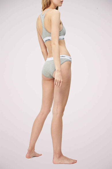 Slip gris de Calvin Klein, avec une ceinture blanche à logo, porté par un modèle avec une nuisette grise assortie.
