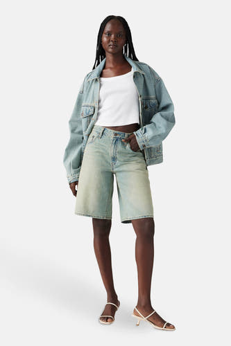 Short en denim bleu clair de Levi's, associé à un chemisier blanc et une veste en denim, dans un style décontracté.