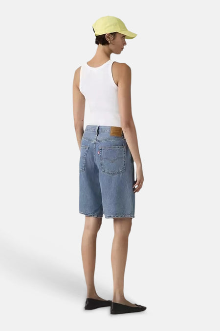 Blauwe mid-lengte denim shorts van Levi's, achterzijde met zakken en label, gedragen met wit tanktop en gele pet