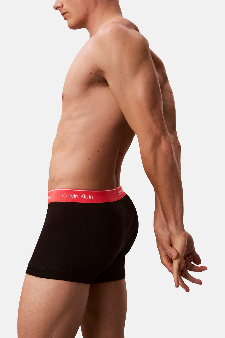 Zwarte boxershort van Calvin Klein, close-up zijwaarts beeld met rode tailleband en een man die zijn handen in elkaar strengelt.
