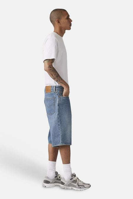 Lichtblauwe denim short van Levi's®, gedragen door een man in een wit T-shirt en grijze sneakers, zij-aanzicht.