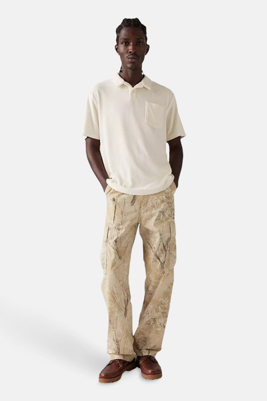 Man met gebroken wit poloshirt en camouflage broek, staand.