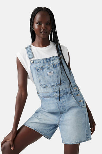 Denim playsuit in lichtblauw van Levi's®, gedragen met een wit mouwloos shirt en zwarte vlechten.