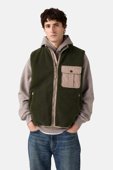 Groene bodywarmer van Levi's, met beige accenten en gedragen over een grijze hoodie met jeans.
