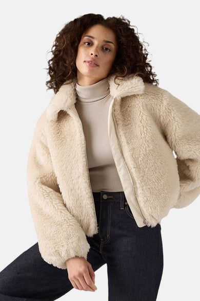 Manteau court beige de Levi's® avec une douce texture, porté sur un gilet beige et des jeans foncés.