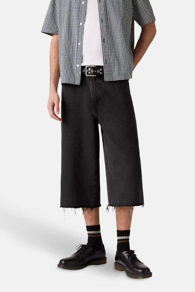 Zwarte jeansshort van denim van Levi's, met gerafelde zoom en gedragen met een geruite blouse.
