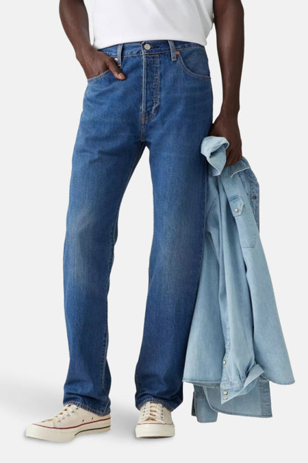 Een man in jeans met een denim overhemd en sneakers.
