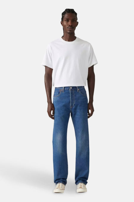 Man in wit T-shirt en blauwe jeans, staand.
