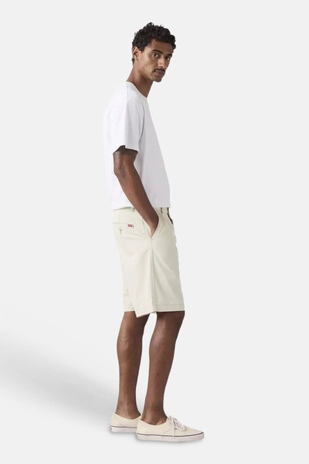 Ecru short van Levi's® in chino-stijl, met rood label op achterzak, gedragen door een man met wit T-shirt en lichte sneakers.