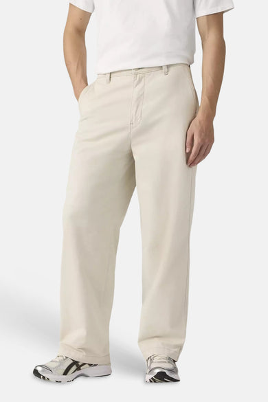 Beige chino van Levi's®, met een wijde pasvorm, gedragen met een wit T-shirt en sportschoenen.