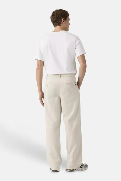 Beige chino met wijde pijpen van Levi's®, met paspelzakken, gedragen door een man met wit T-shirt en sneakers.
