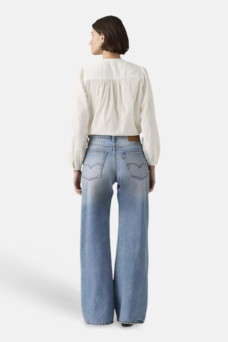 Lichtblauwe denim bootcut jeans van Levi's® met een lichte washing, wijde pijpen en zichtbare stiksels op de achterzakken, van achteren gedragen door een model met een witte blouse.