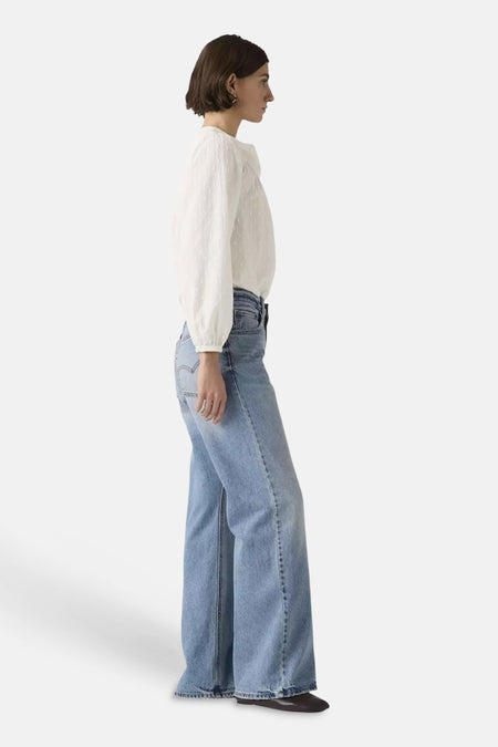 Lichtblauwe bootcut jeans van Levi's® met wijde pijpen, gedragen door een model in een wit gestippeld shirt, in zijprofiel.