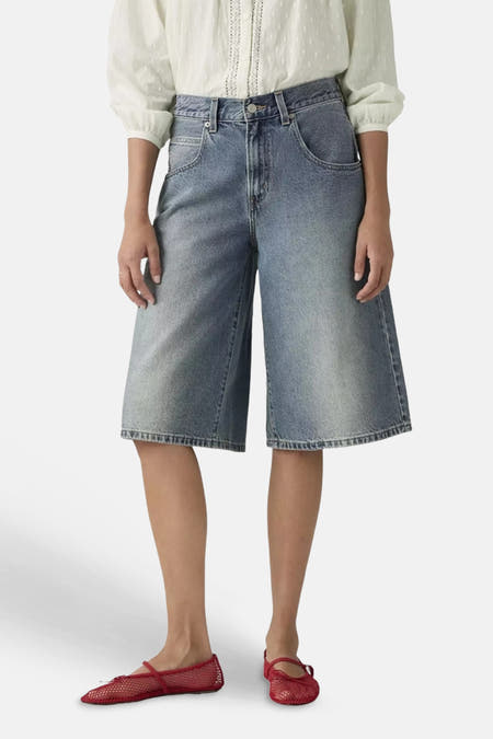 Midblauwe denim short van Levi's® met wijde pijpen, gedragen met een witte blouse en rode netballetschoenen.