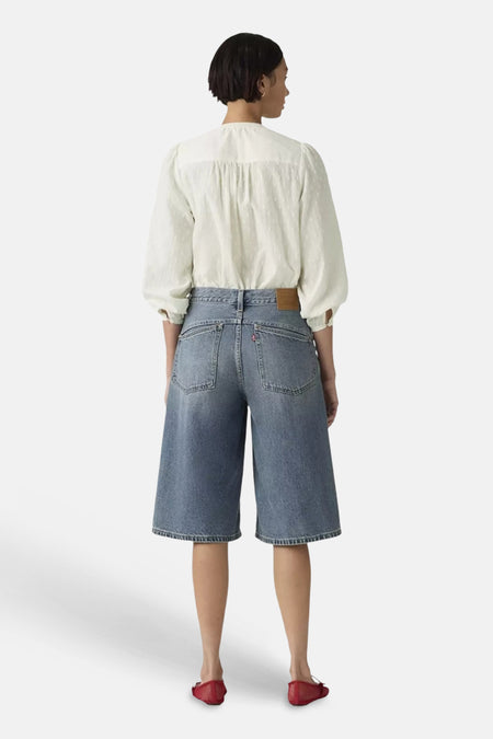 Mid blauwe denim short van Levi's® met wijde pijpen, achterzakken en een leren patch, achteraanzicht, gedragen met een witte blouse en rode flats.