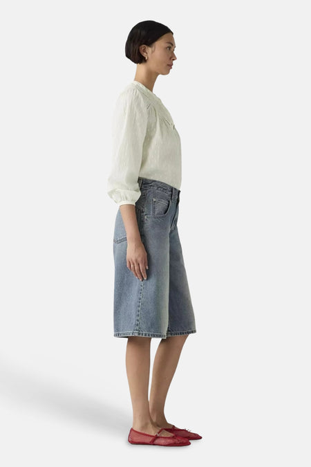Mid-blauwe denim short van Levi's® met wijde pijpen, getoond in zijaanzicht met een witte blouse en rode balletschoenen.