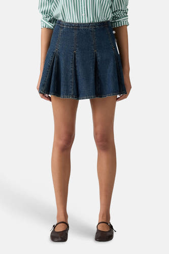 Donkerblauwe denim korte rok van Levi's® met plooien, gedragen door een model met een gestreept overhemd en donkere Mary Jane schoenen.