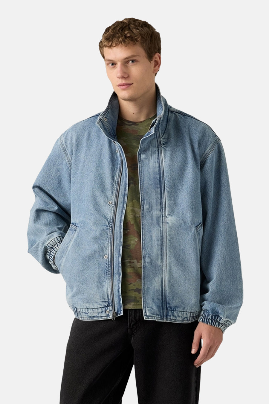 Korte denim jas van Levi's, met een ritssluiting en gedragen over een camouflage T-shirt, gecombineerd met een zwarte broek.
