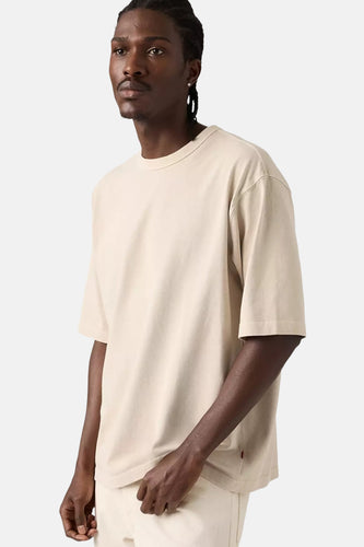 Beige T-shirt met korte mouwen van Levi's, gedragen door een model met gevlochten haar en een zilveren oorbel.