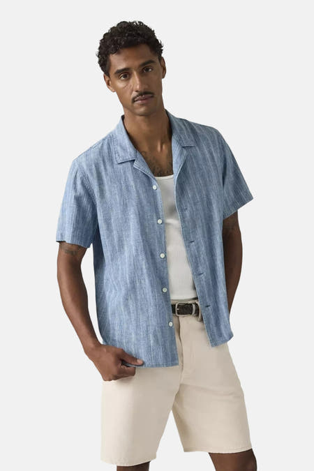 Blauw hemd met korte mouwen van Levi's® met subtiele verticale streeptextuur, campkraag, gedragen over een wit hemd en beige korte broek.