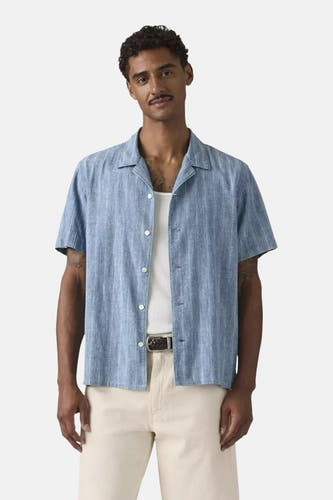 Blauw overhemd met korte mouwen van Levi's®, met fijne verticale textuur, open over een wit hemdje en crèmekleurige broek.