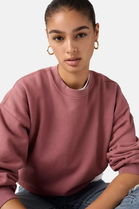 Roze sweater met ronde hals van Levi's®, gedragen met gouden oorringen en een wit shirt eronder.
