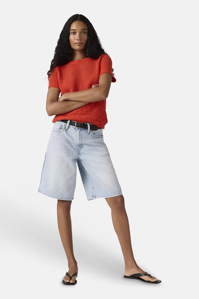 Lichtblauwe denim short van Levi's®, gedragen door een model met een rode gebreide top, zwarte riem en teenslippers.