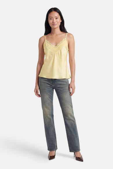 Haut en satin jaune de Terra di Siena à fines bretelles, vu de dos sur un mannequin portant un jean gris et des talons.