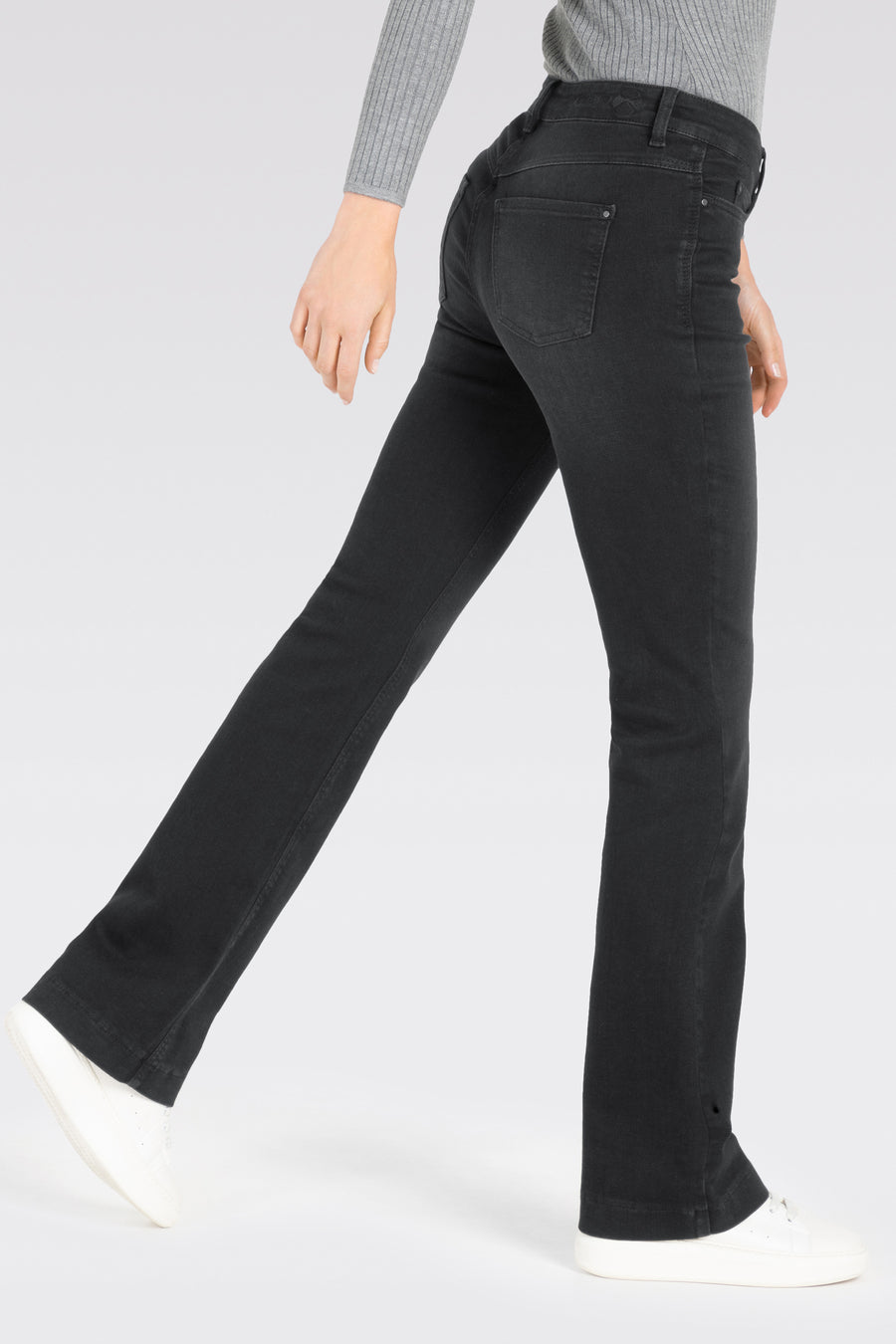 Donkergrijze bootcut jeans van MAC, met subtiele details en gedragen met witte sneakers en een grijze trui.
