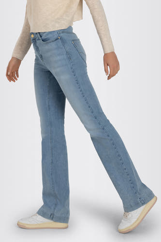 Jean bootcut bleu clair en denim de MAC, avec un pull beige et des baskets blanches.