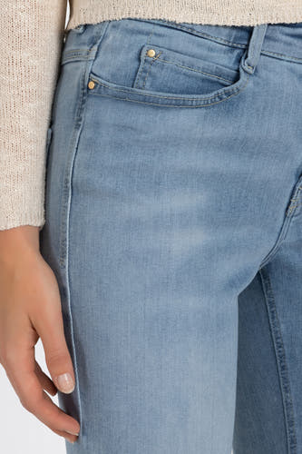 Lichtblauwe bootcut jeans van MAC, met zakdetail en een hand zichtbaar.