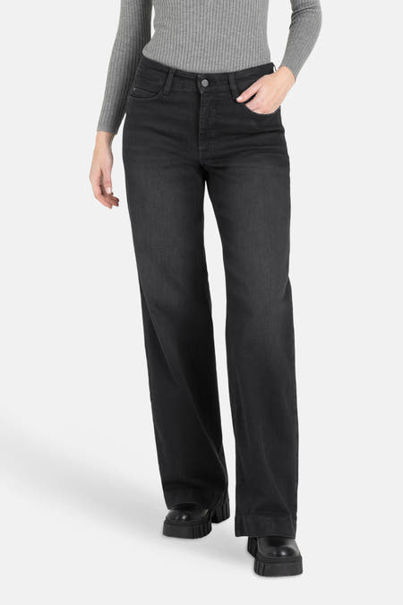 Jean boyfriend noir de MAC, avec une main dans la poche et associé à un pull gris et des chaussures noires.