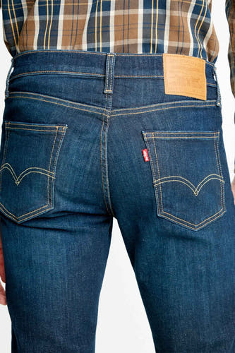 Jean slim fit bleu marine de Levi's, avec des poches arrière caractéristiques et un logo rouge, porté avec une chemise à carreaux.