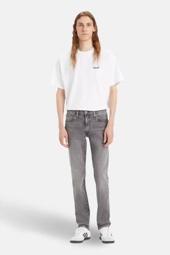 Jean slim fit léger gris de Levi's, porté avec un t-shirt blanc et des baskets blanches à rayures noires.