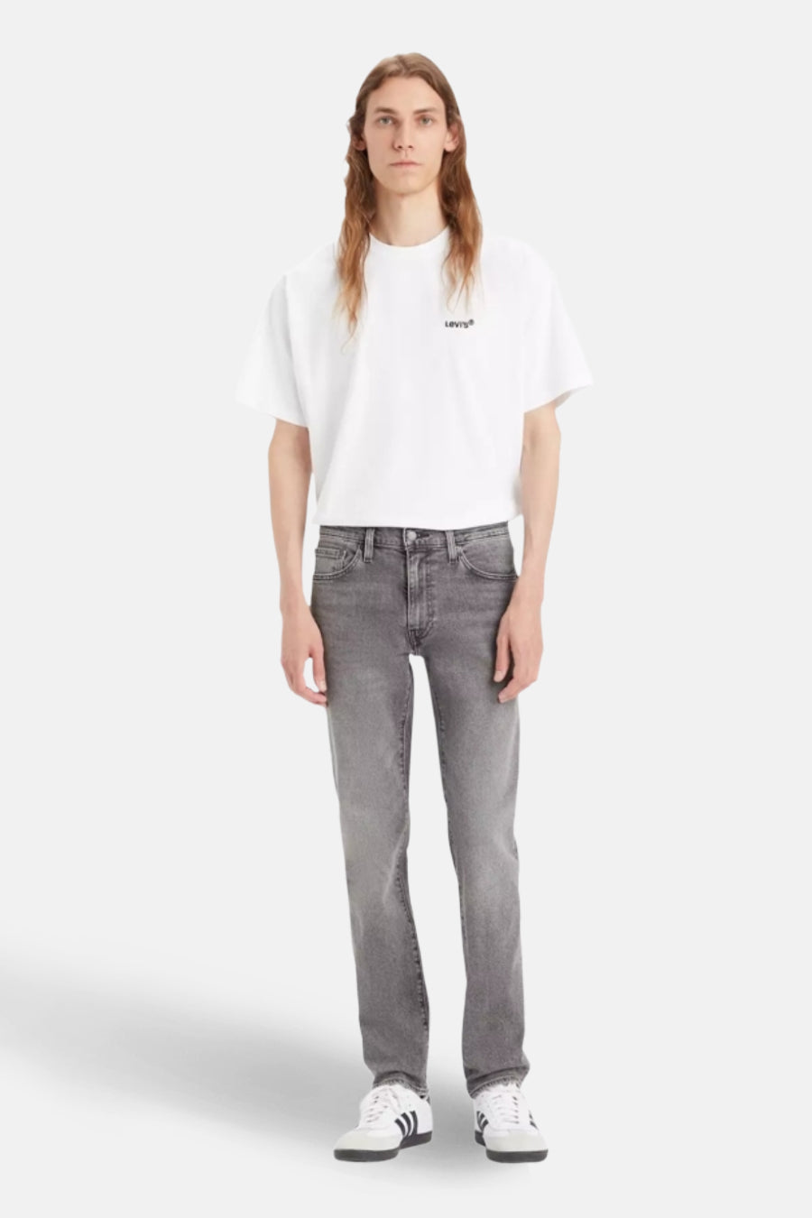 Man in witte T-shirt, grijze jeans en Adidas sneakers.
