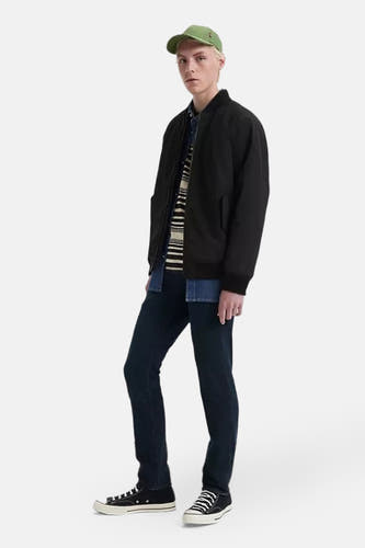 Jean slim en denim bleu marine de Levi's®, associé à une veste bomber noire, un t-shirt rayé et des baskets noires.