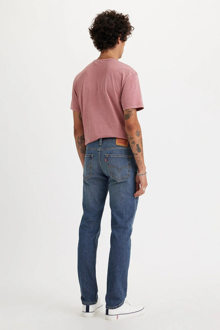 Mid blue slim-fit jeans van Levi's® met vervaagde was, achterzakken en rits, gezien van achteren op model in roze t-shirt en witte sneakers.