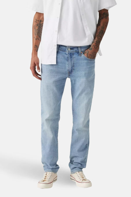 Slim jeans van lichtblauw denim van Levi's, met een open wit overhemd en crèmekleurige sneakers.
