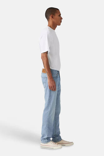 Lichtblauwe slim jeans van Levi's, gezien vanaf de zijkant, gecombineerd met een wit T-shirt en crèmekleurige sneakers.
