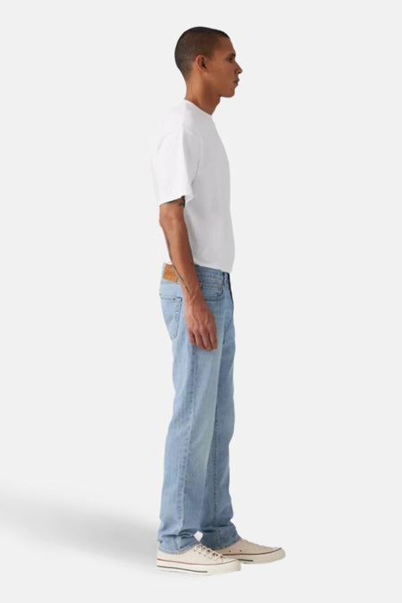 Jean slim de denim bleu clair de Levi's, vu de du côté, associé à un T-shirt blanc et des baskets blanches.