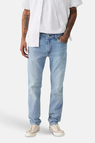 Lichtblauwe slim jeans van Levi's, gedragen met een wit t-shirt en een open wit overhemd en crèmekleurige sneakers.