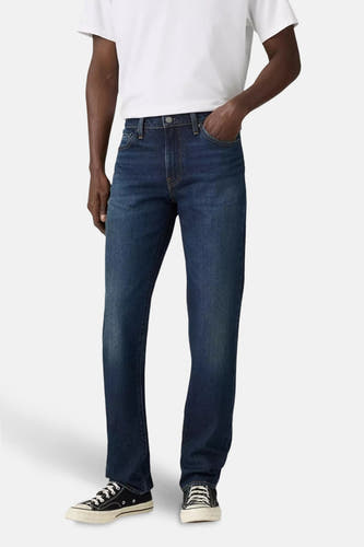 Donkerblauwe slim fit jeans van Levi's, gedragen met een wit T-shirt en zwarte canvas schoenen.
