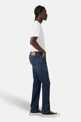 Slim fit jeans van donkerblauw denim van Levi's, met een witte T-shirt en zwarte schoenen, in zijaanzicht.