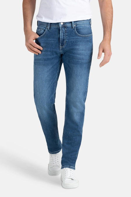 Middenblauwe rechte jeans van MAC, met subtiele wassing en witte stiksels, gecombineerd met witte sneakers en een wit T-shirt.
