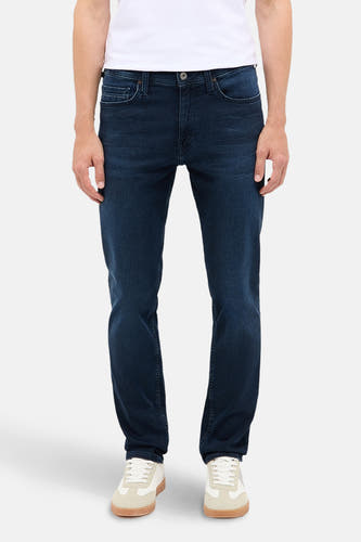 Jean slim fit bleu marine de MUSTANG, porté avec un T-shirt blanc et des baskets crème.