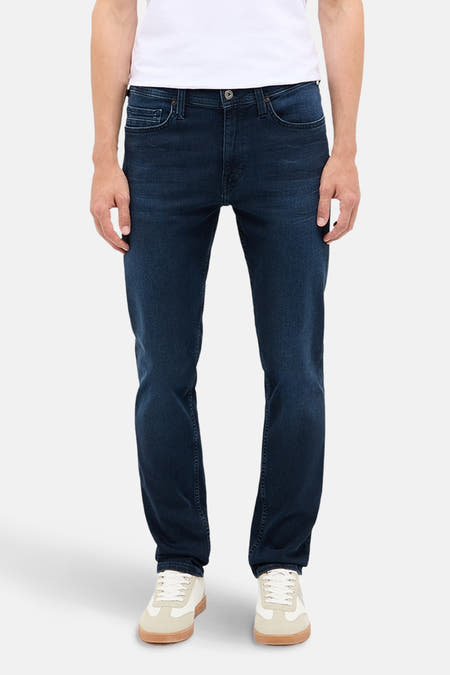 Jean slim fit bleu marine de MUSTANG, porté avec un T-shirt blanc et des baskets crème.