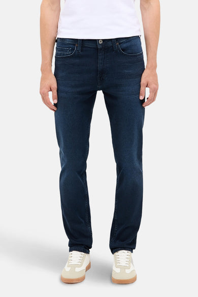 Jean slim fit bleu marine de MUSTANG, porté avec un T-shirt blanc et des baskets crème.