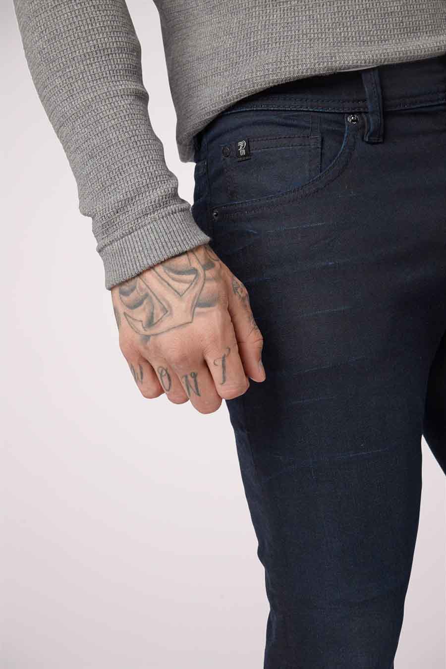 Slim fit blauw-zwarte denim jeans van TOM TAILOR, met tatoeages op de hand, en een grijze trui.
