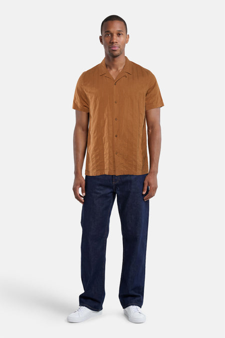 Bruin overhemd met korte mouwen van BEN SHERMAN met subtiele verticale streeptextuur en reverskraag, gedragen met een donkerblauwe jeans en witte sneakers.