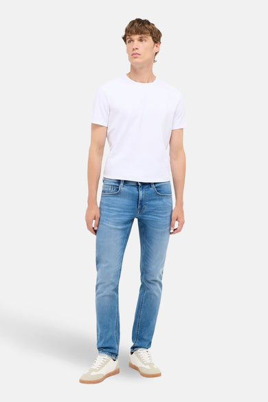 Slim fit jeans van lichtblauw denim van MUSTANG, met witte t-shirt en crèmekleurige sneakers.
